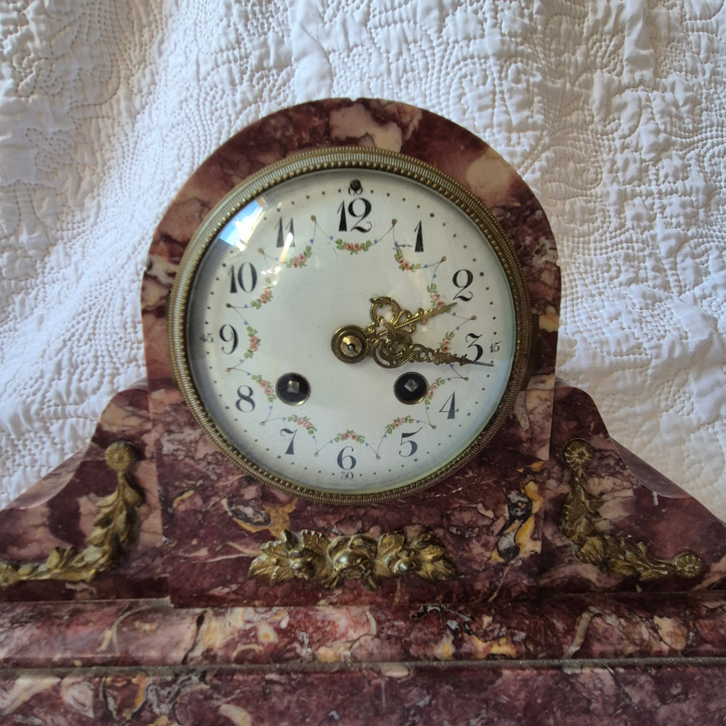 Détail réel du cadran floral et des ornements dorés de la pendule en marbre rouge.
