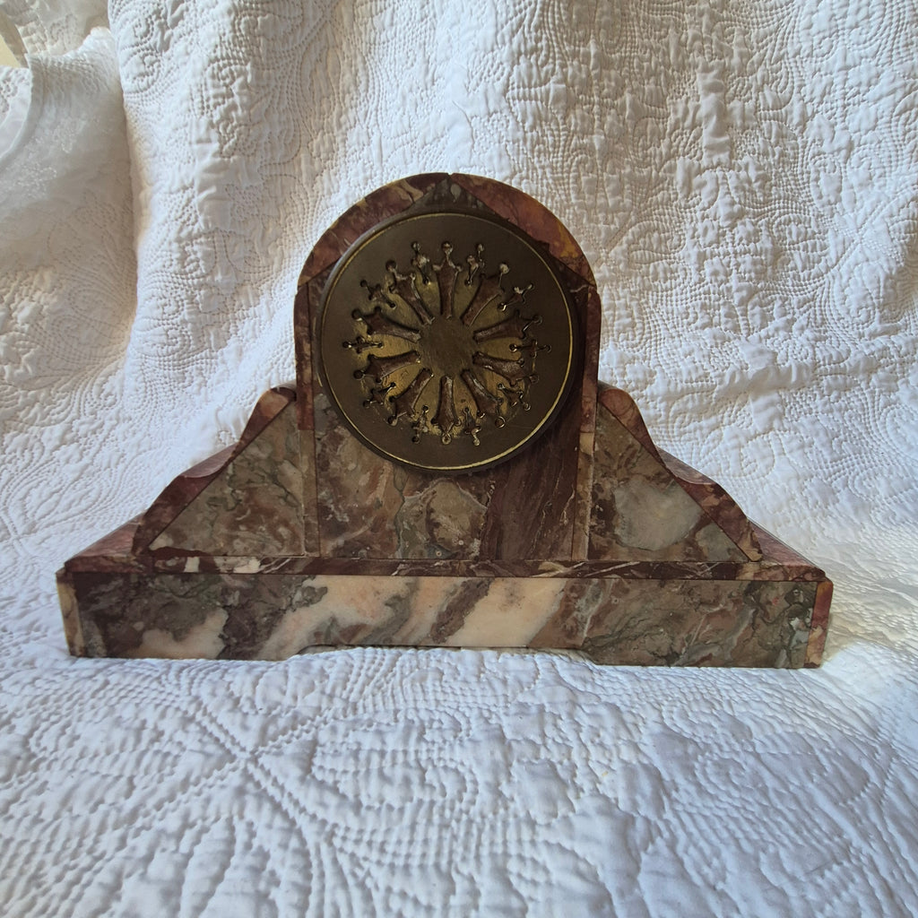 Vue réelle de l’arrière de la pendule en marbre rouge et de sa trappe circulaire ouvragée.
