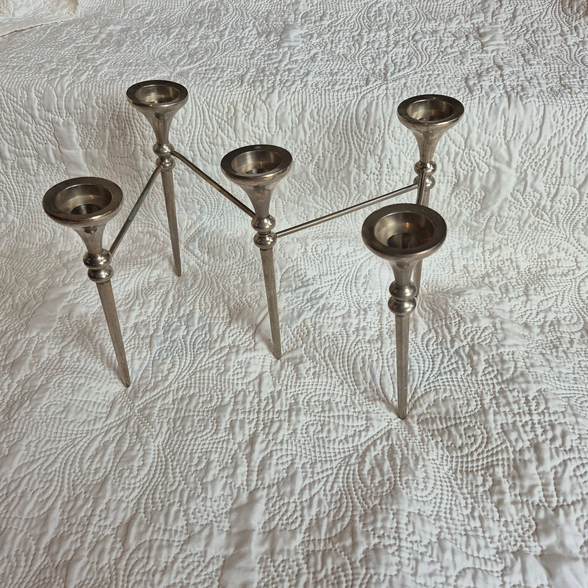 Vue légèrement plongeante du chandelier déployé en zigzag, montrant l’intérieur des cinq coupelles sur un tissu blanc.
