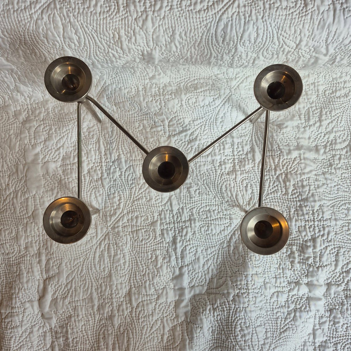 Chandelier vu du dessus : les cinq coupelles et les bras mobiles forment un zigzag sur le tissu blanc.