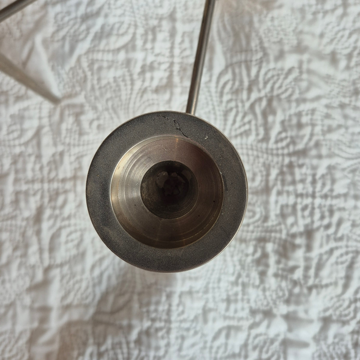 Gros plan du dessus d’une coupelle du chandelier, montrant son logement à bougie, sa patine et les marques sur le bord.